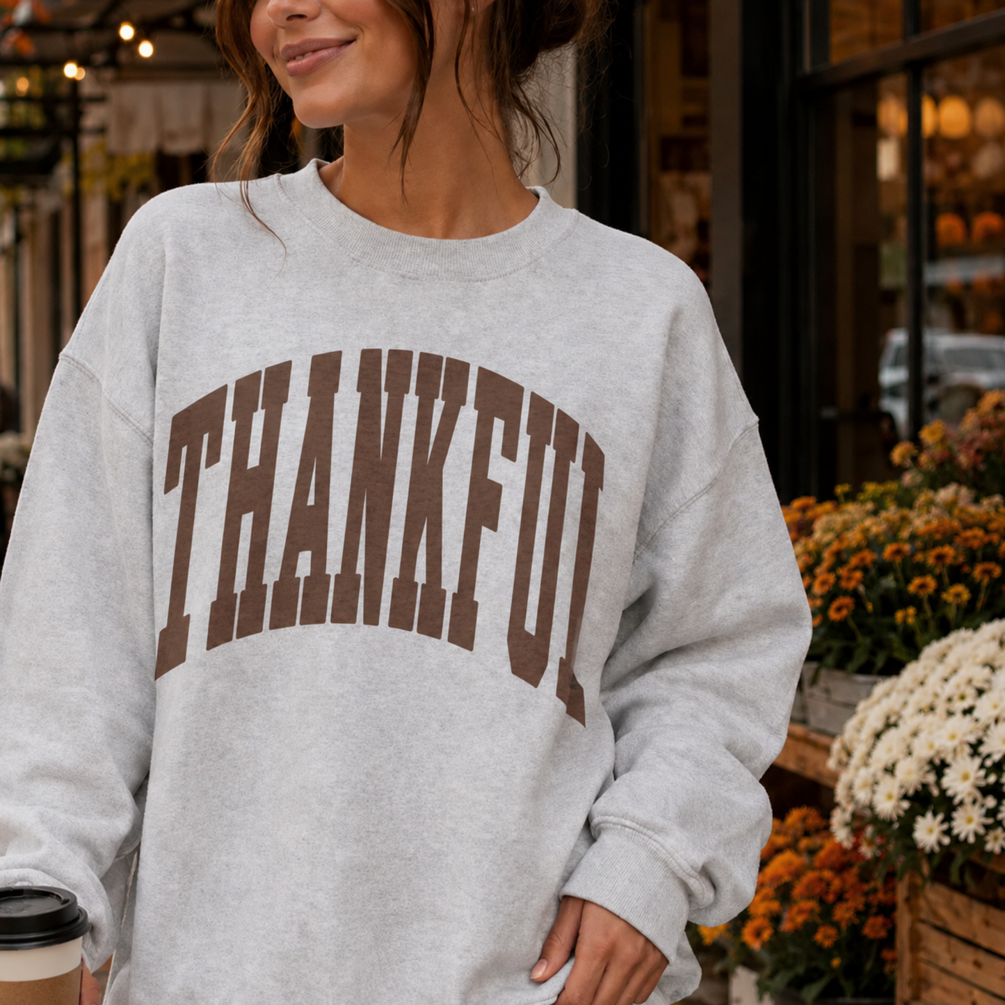 Woman wearing oatmeal heather Thankful graphic sweatshirt with brown collegiate lettering for a cozy fall outfit