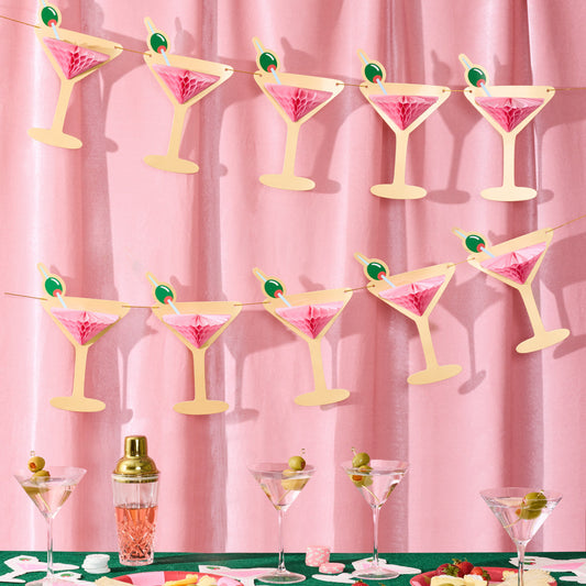 Decorative martini glass banner with pink and green decorations on a pink curtain background.