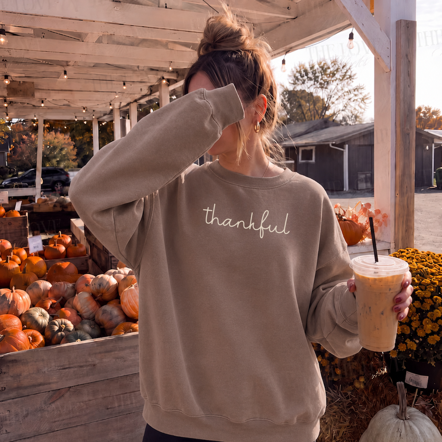 Woman wearing neutral Thankful script crewneck sweatshirt at a fall pumpkin patch with iced coffee