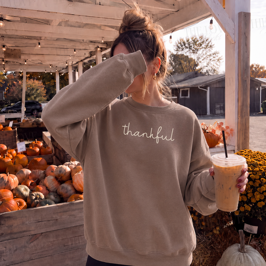Woman wearing neutral Thankful script crewneck sweatshirt at a fall pumpkin patch with iced coffee