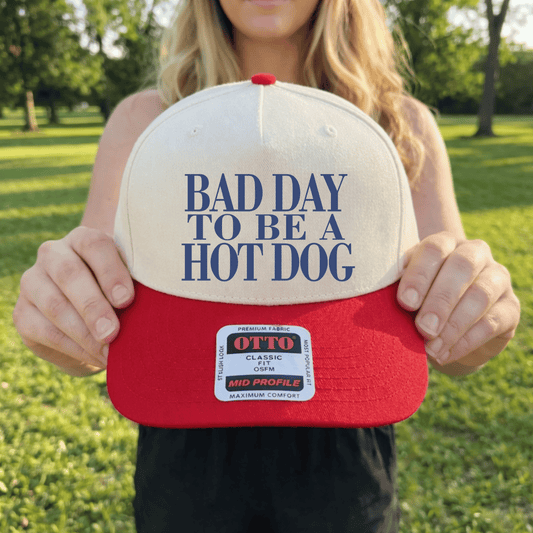 Bad Day to Be a Hot Dog OTTO baseball cap with red bill and canvas crown held outdoors in summer setting