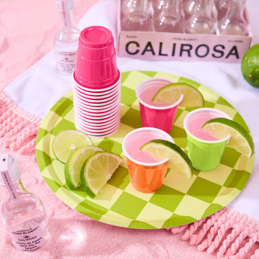 Party setup with pink cups, lime slices, and 'Calirosa' bottles on a checkered plate.