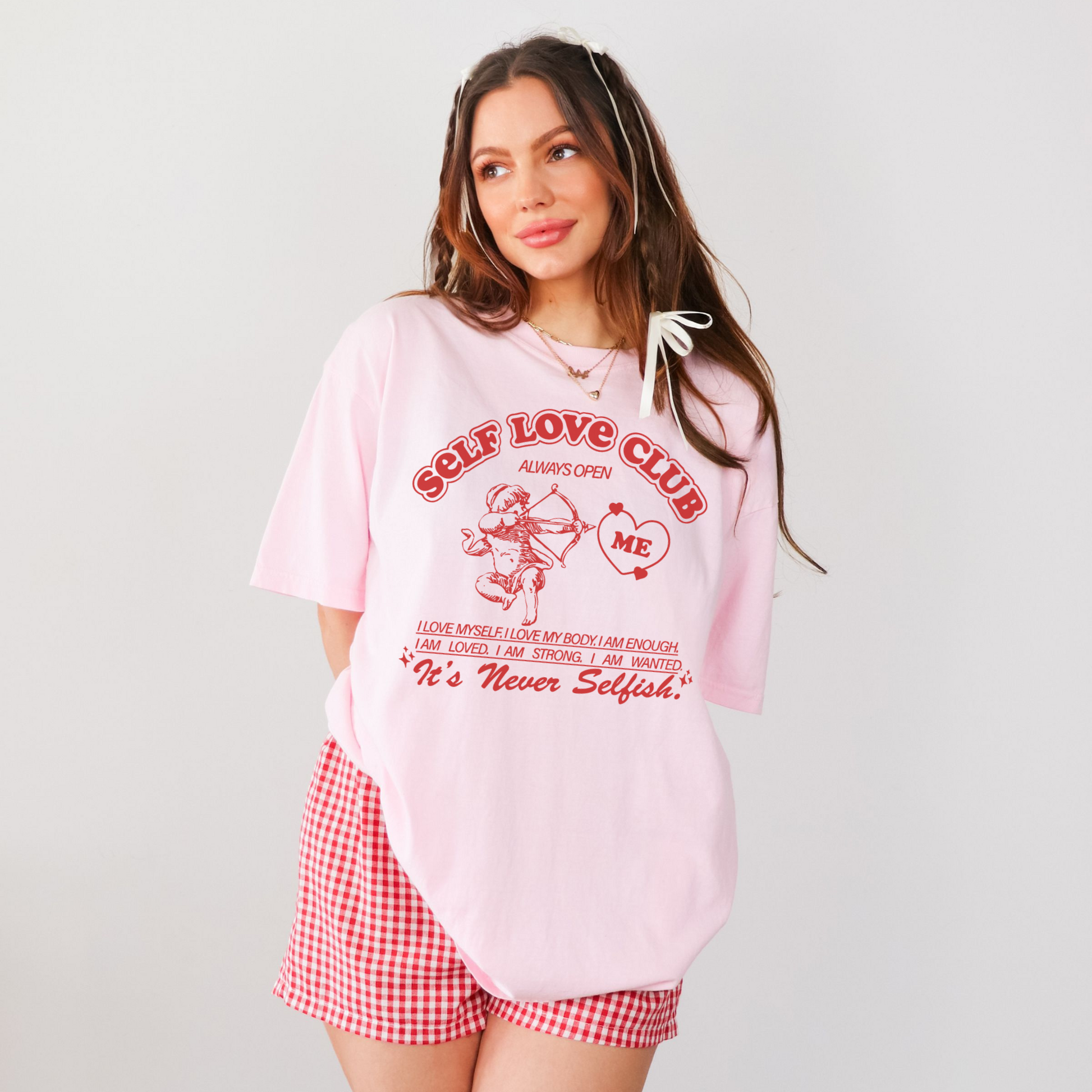Model wearing blush pink oversized Self Love Club graphic tee styled with red gingham shorts