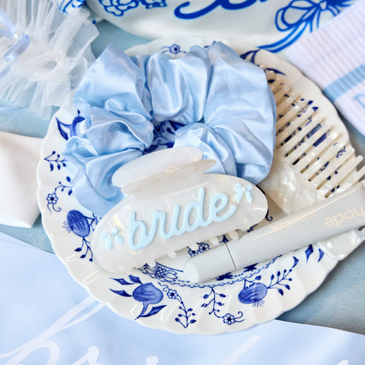 Blue scrunchie and hairbrush on a decorative plate with 'bride' text, on a matching blue background.