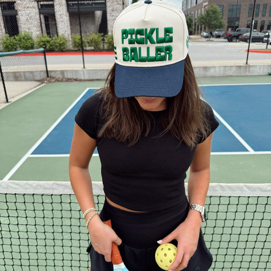 Person wearing a 'Pickle Baller' cap on a tennis court