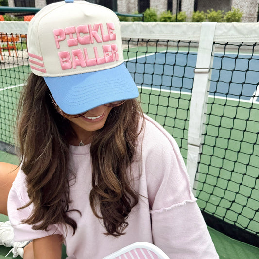 Woman wearing a cap with 'Pickle Baller' on a tennis court
