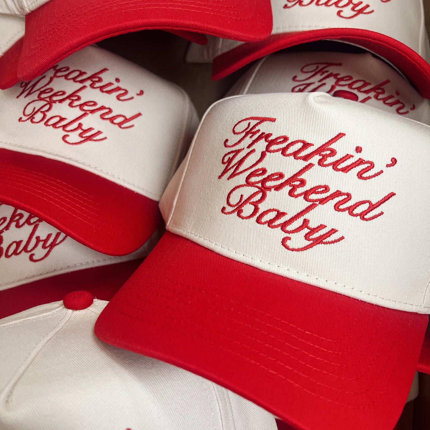 Red and white caps with 'Freakin' Weekend Baby' text on a brown background