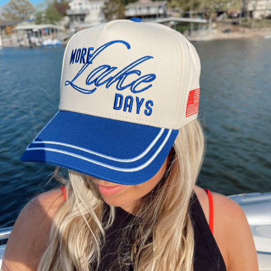 Person wearing a cap with 'More Lake Days' text by a lake