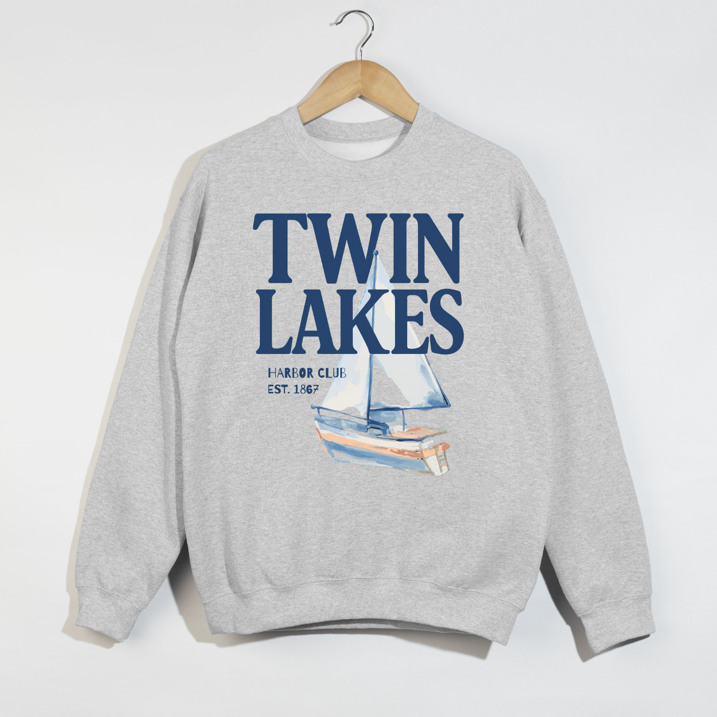 Twin Lakes Harbor Club crewneck sweatshirt featuring large navy lettering and watercolor sailboat artwork on a heather gray sweatshirt.