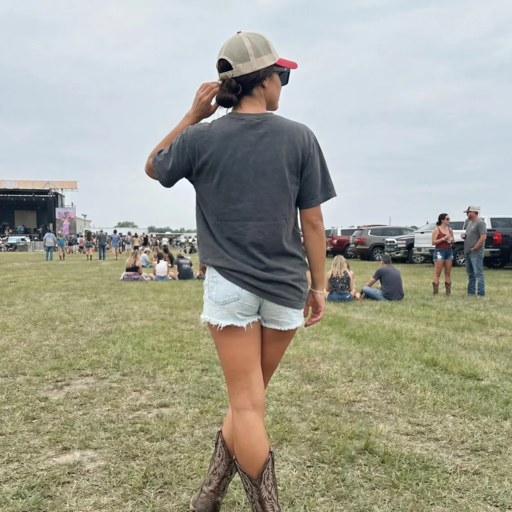woman wearing support live music shirt from back at country concert western outfit denim shorts boots festival look