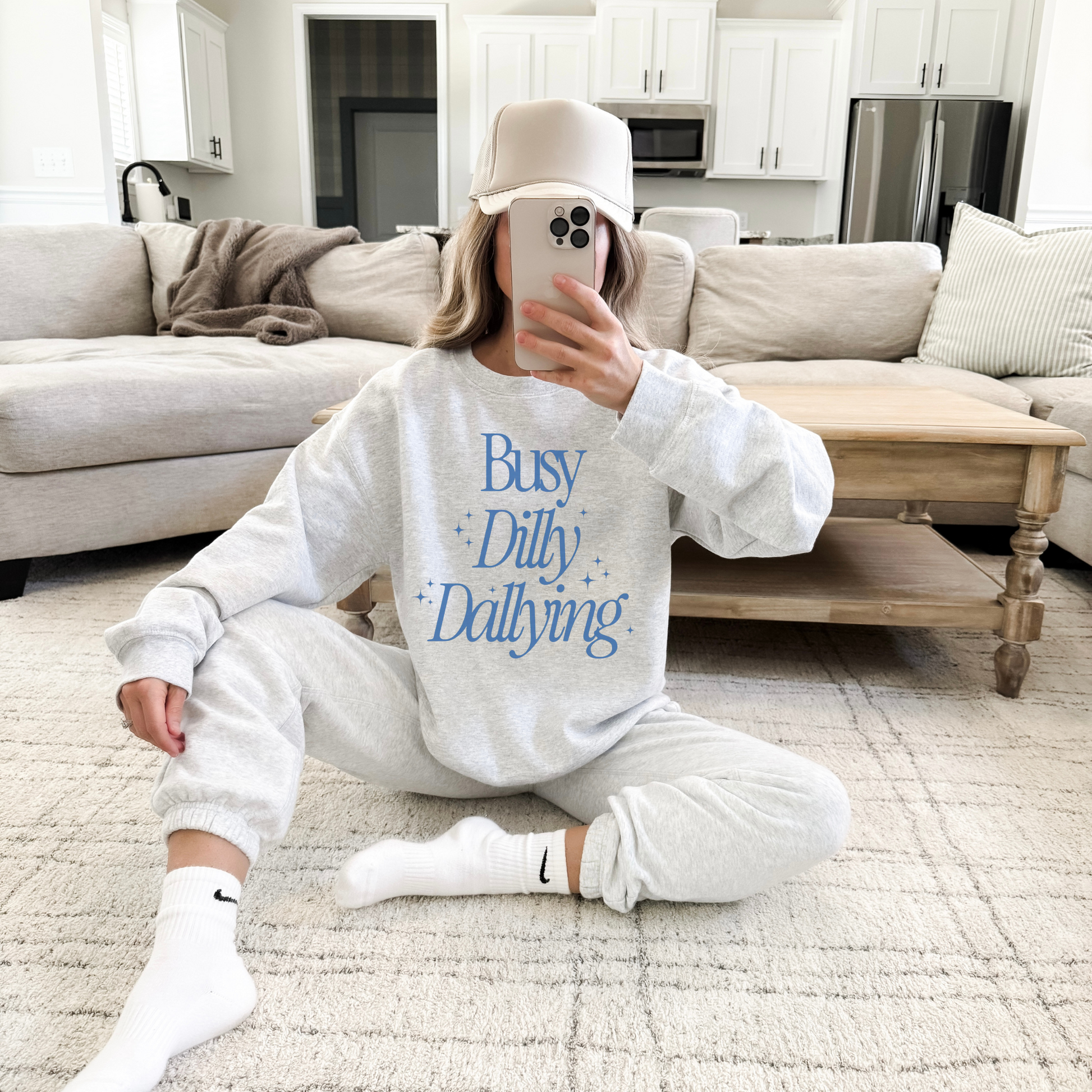 Person wearing a 'Busy Dilly Dallying' sweatshirt in a living room.