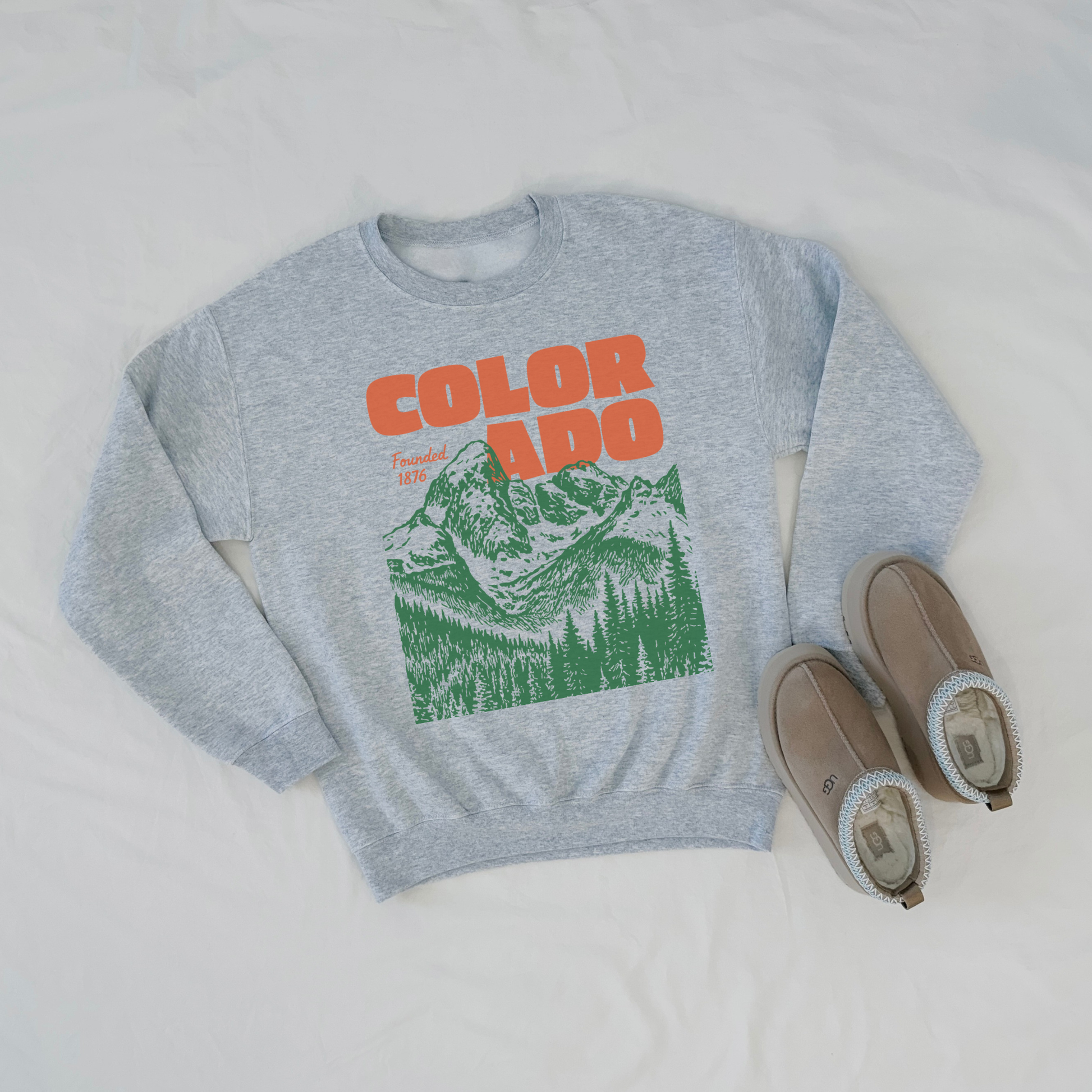 Gray sweatshirt with 'COLORADO' and mountain graphic, paired with brown slippers on a light gray background