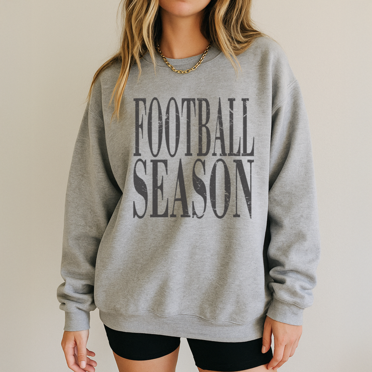 Gray sweatshirt with 'FOOTBALL SEASON' text worn by a person on a beige background