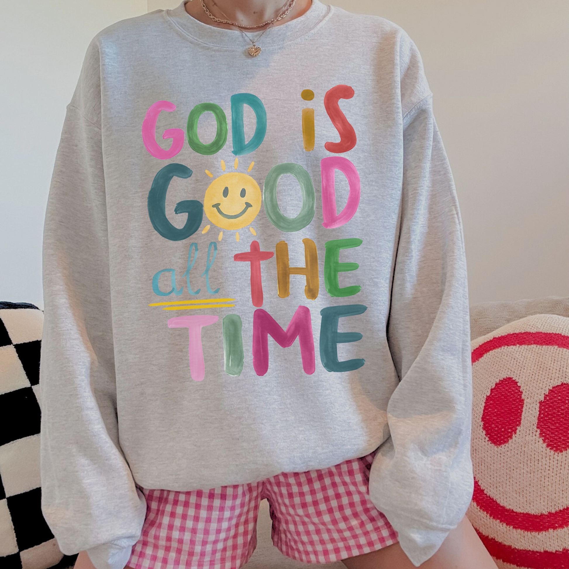 Person wearing a gray sweatshirt with colorful text and checkered shorts, sitting on a couch.