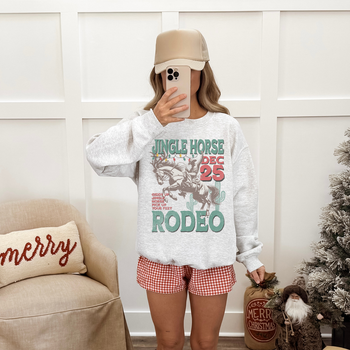 Person wearing a festive sweatshirt with 'Jingle Horse Rodeo' text in a living room setting.