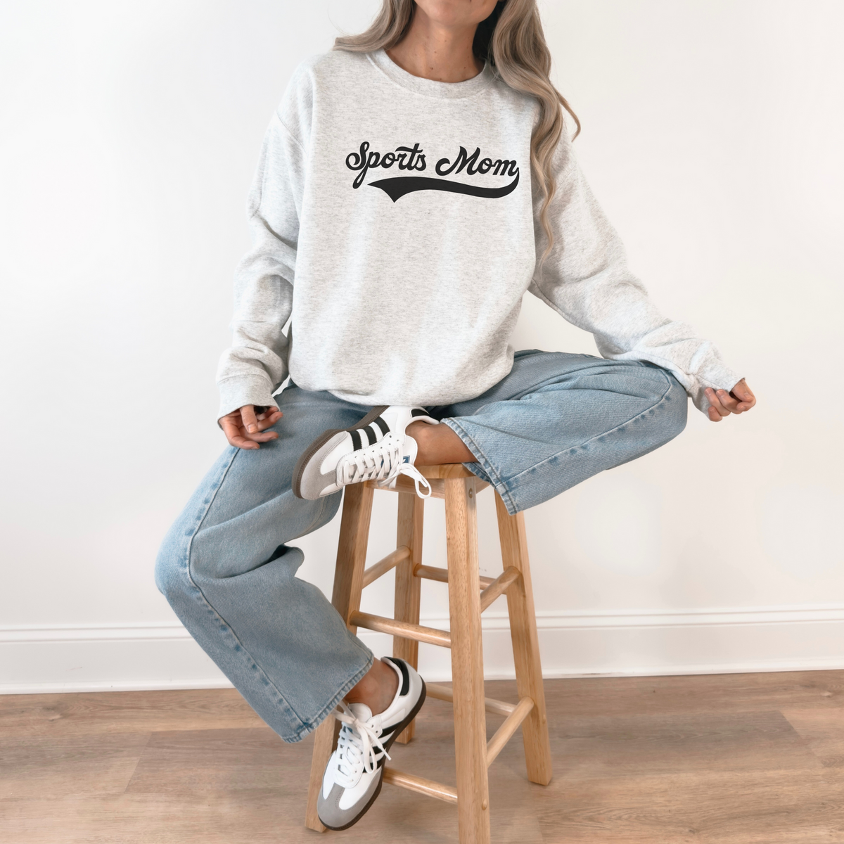 Person wearing a 'Sports Mom' sweatshirt sitting on a wooden stool.