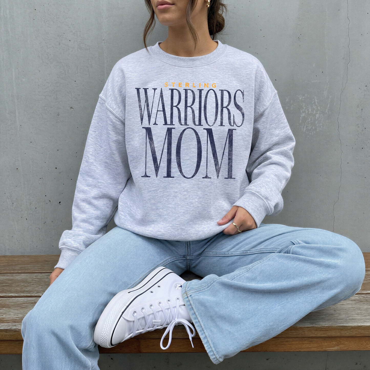 Sterling Warriors Mom gray crewneck sweatshirt worn by woman sitting casually with jeans relaxed cozy outfit