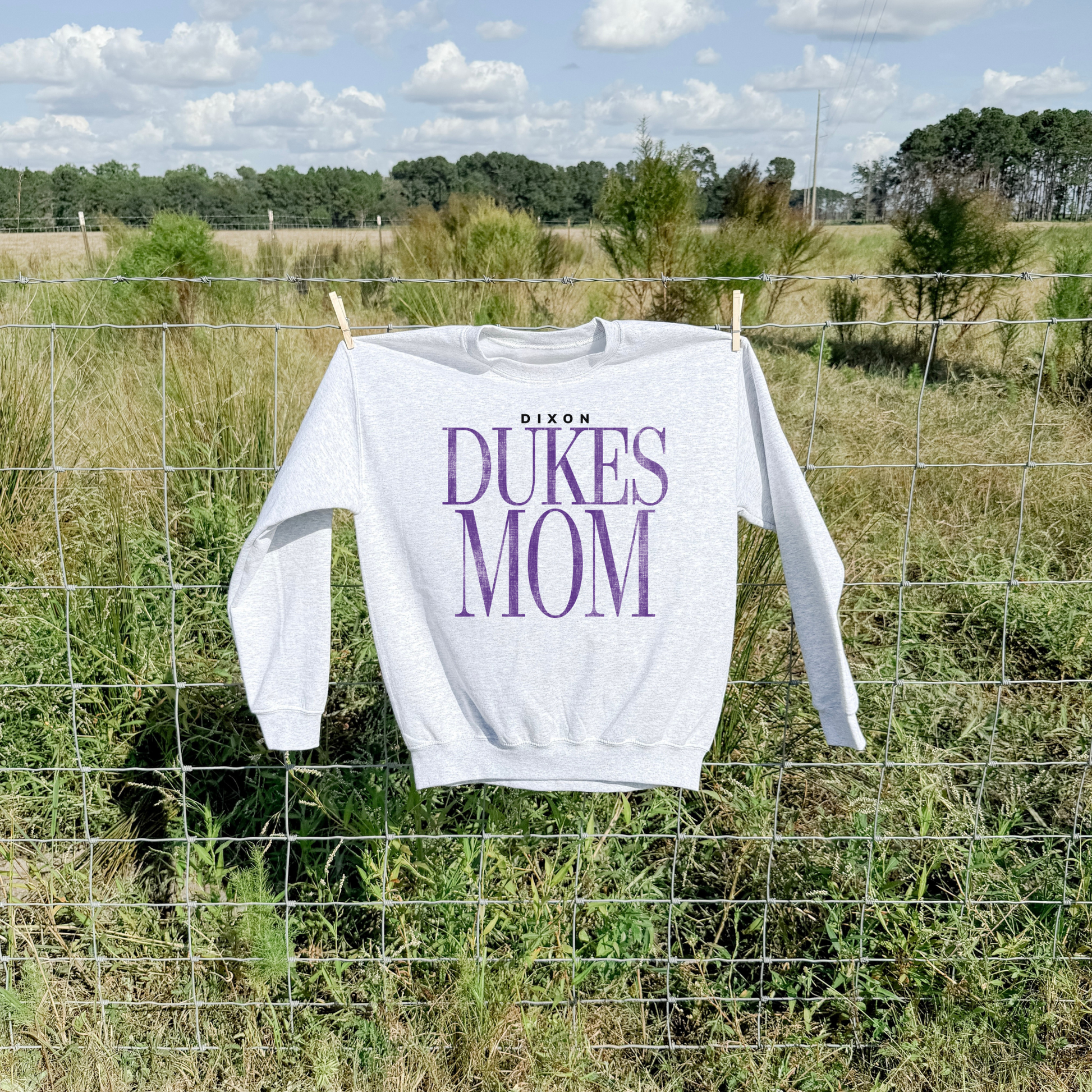Ash grey Dixon Dukes Mom sweatshirt hanging on fence outdoors lifestyle product image