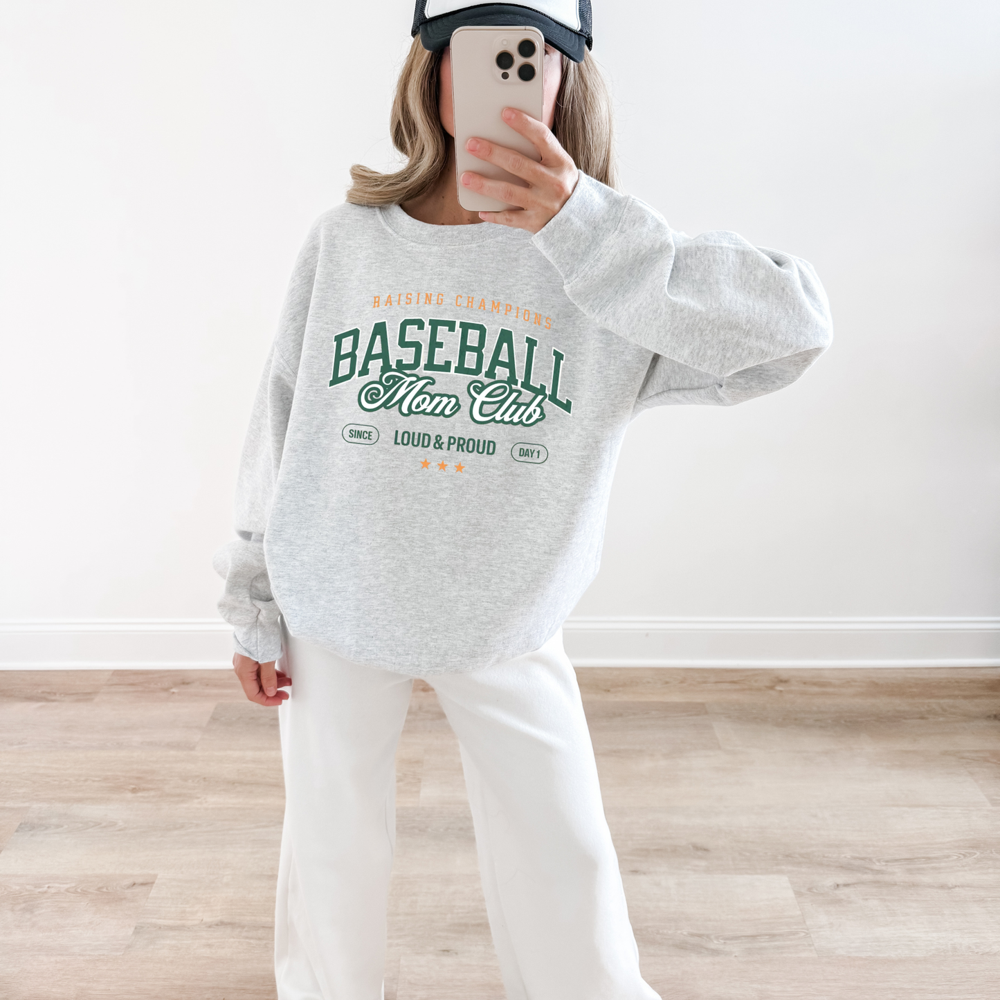 Woman wearing an ash grey “Baseball Mom Club” crewneck sweatshirt taking a mirror selfie.