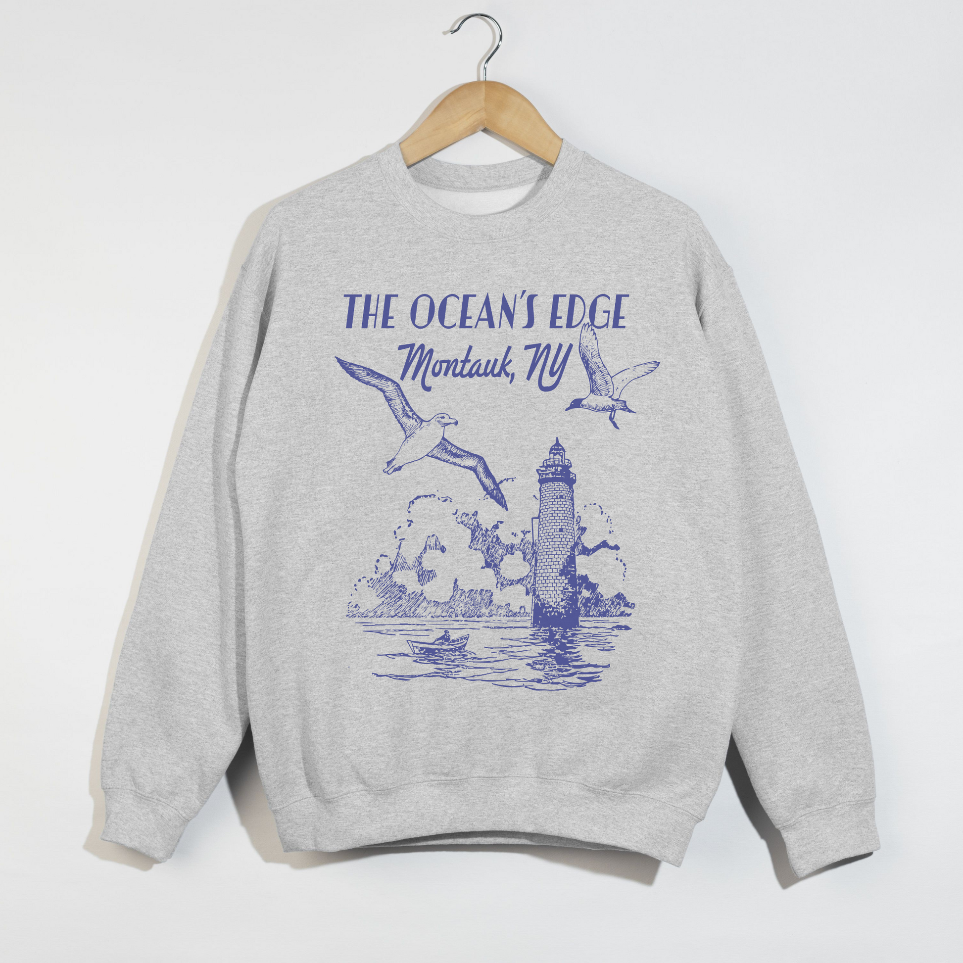 "Ash grey sweatshirt with blue Montauk lighthouse and seagulls coastal design displayed on hanger."