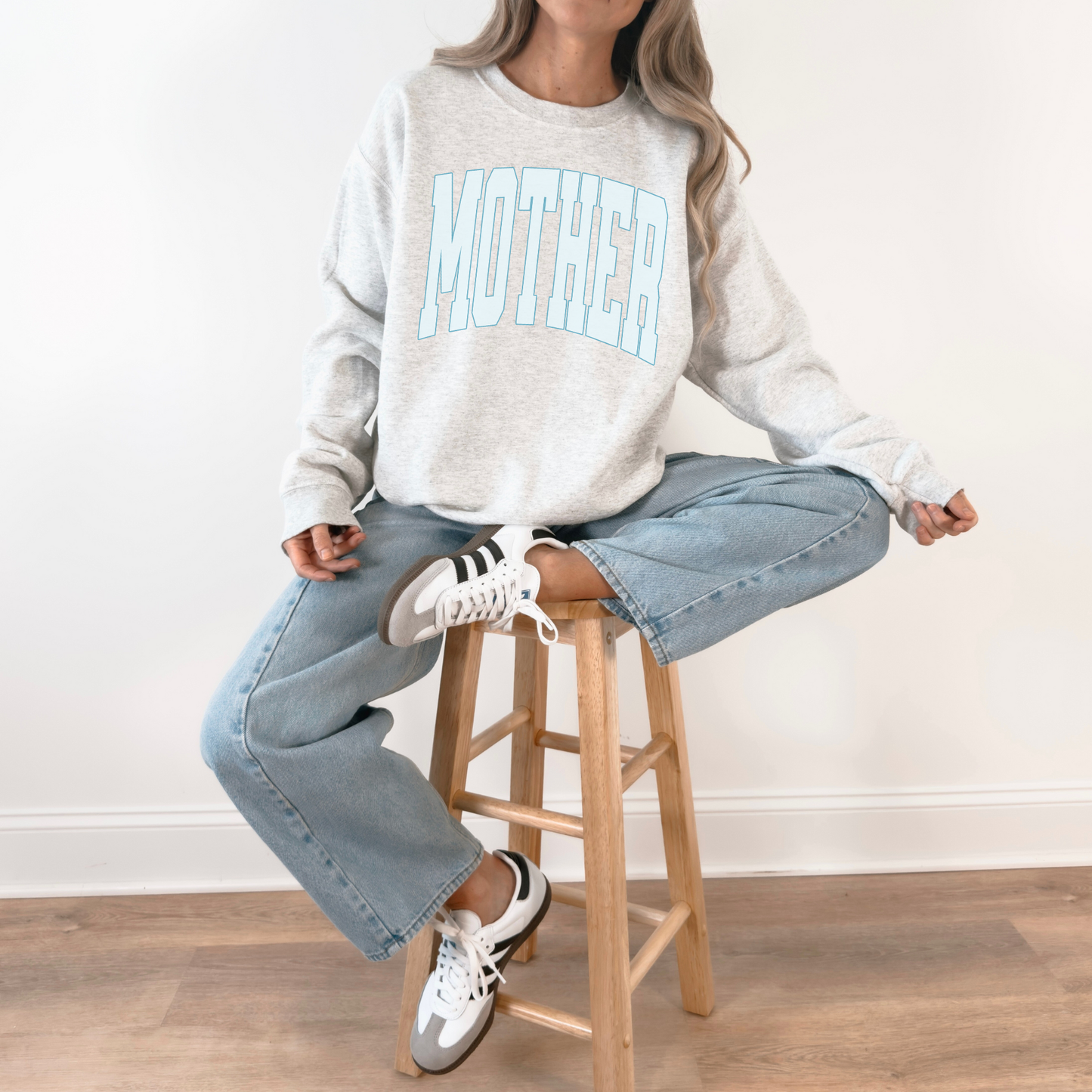 Grey MOTHER crewneck sweatshirt worn casually with jeans while seated on stool