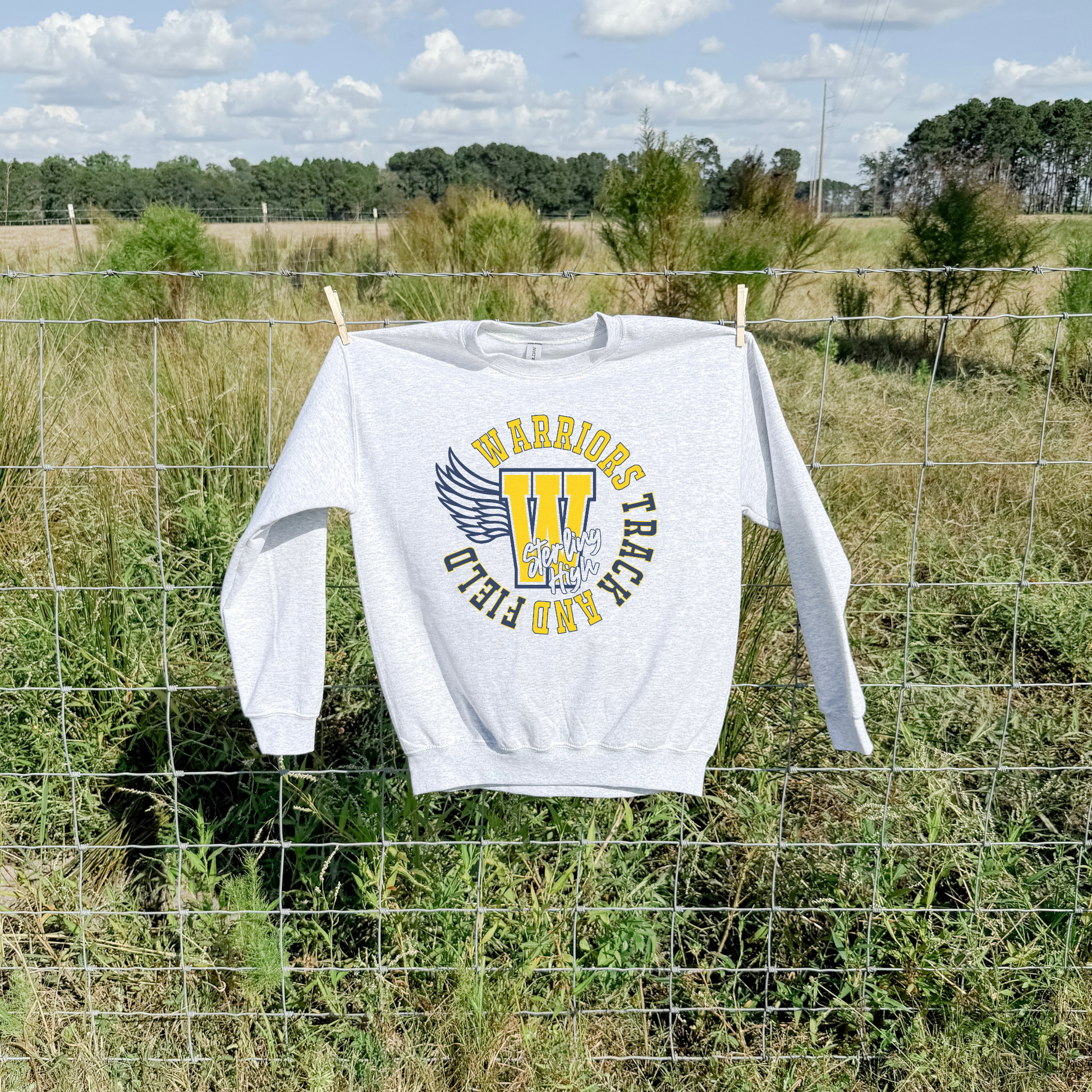 Sterling High Warriors Track and Field crewneck sweatshirt hanging outdoors on fence