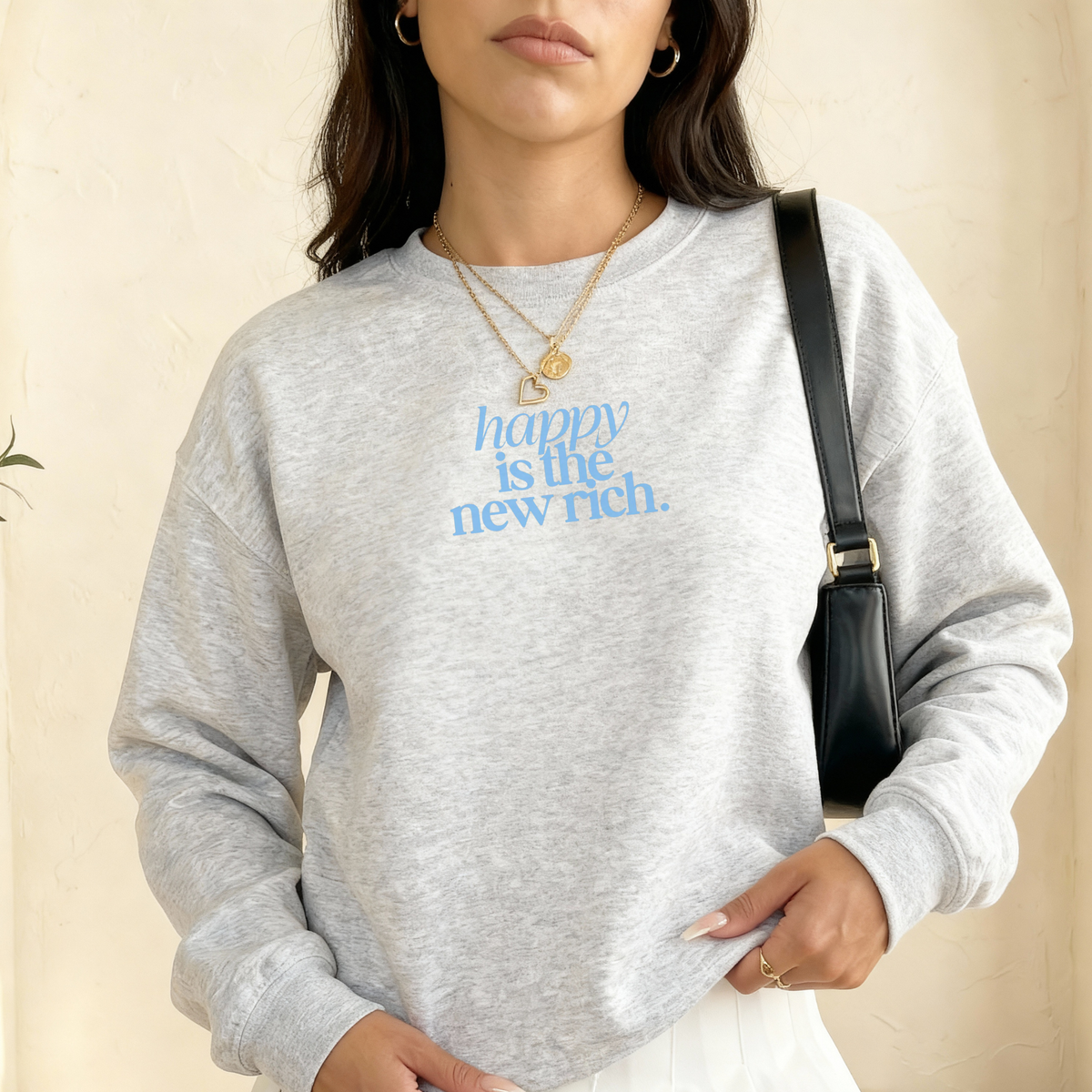 Woman wearing ash grey sweatshirt with blue “happy is the new rich.” text graphic styled casually