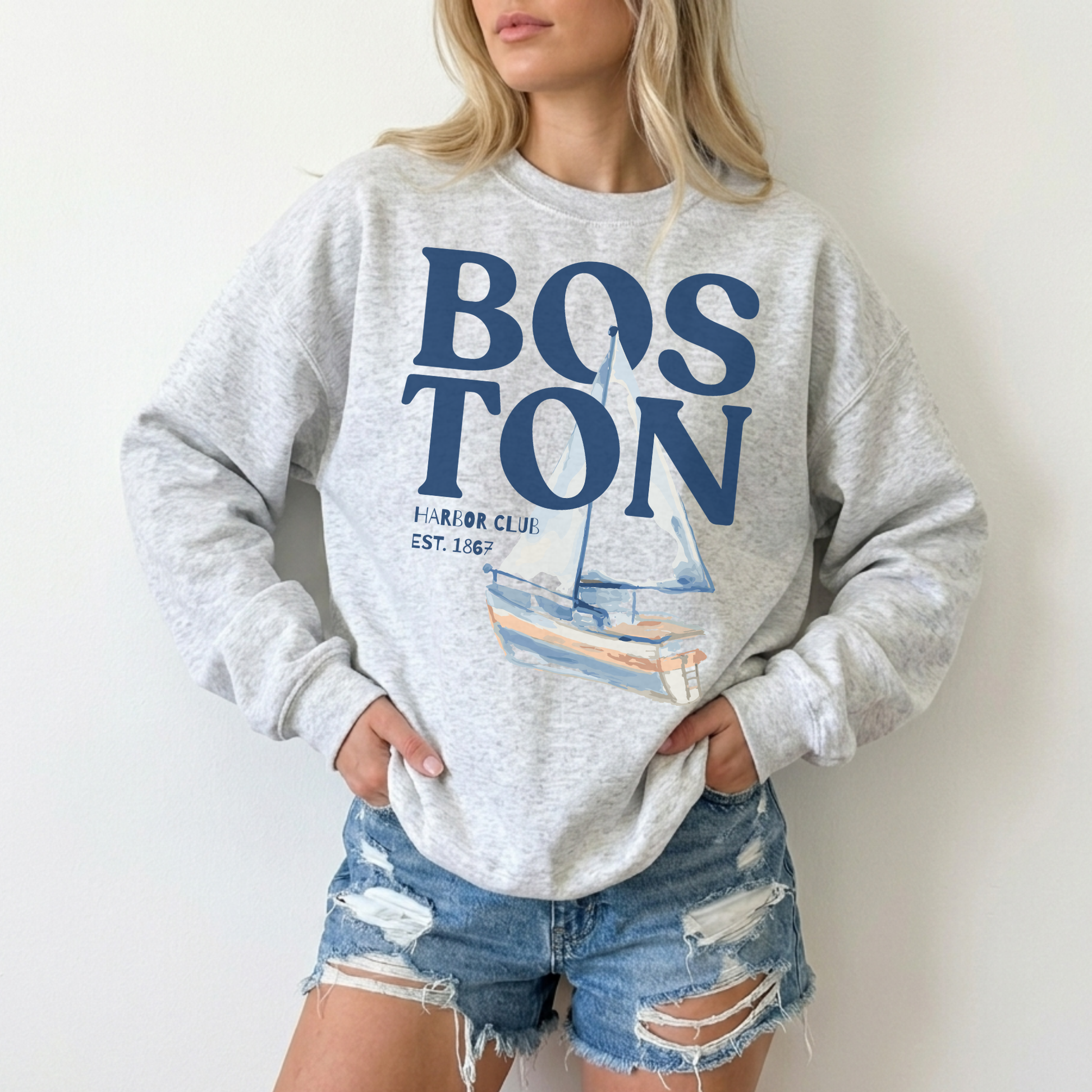Woman wearing ash grey Boston Harbor Club vintage sailboat sweatshirt with denim shorts casual coastal outfit