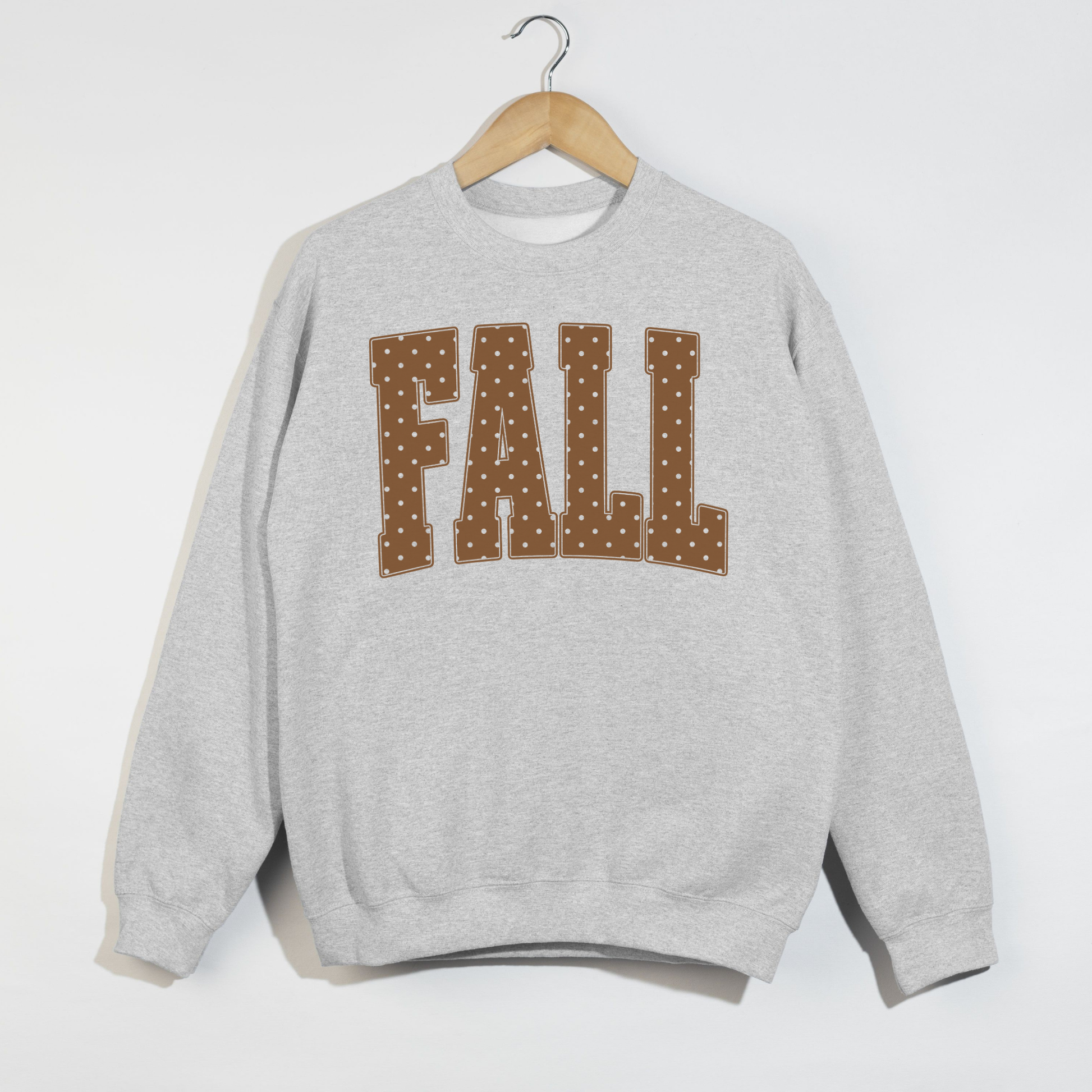 Ash grey crewneck sweatshirt featuring oversized brown polka dot "FALL" lettering in a collegiate-inspired design for autumn.