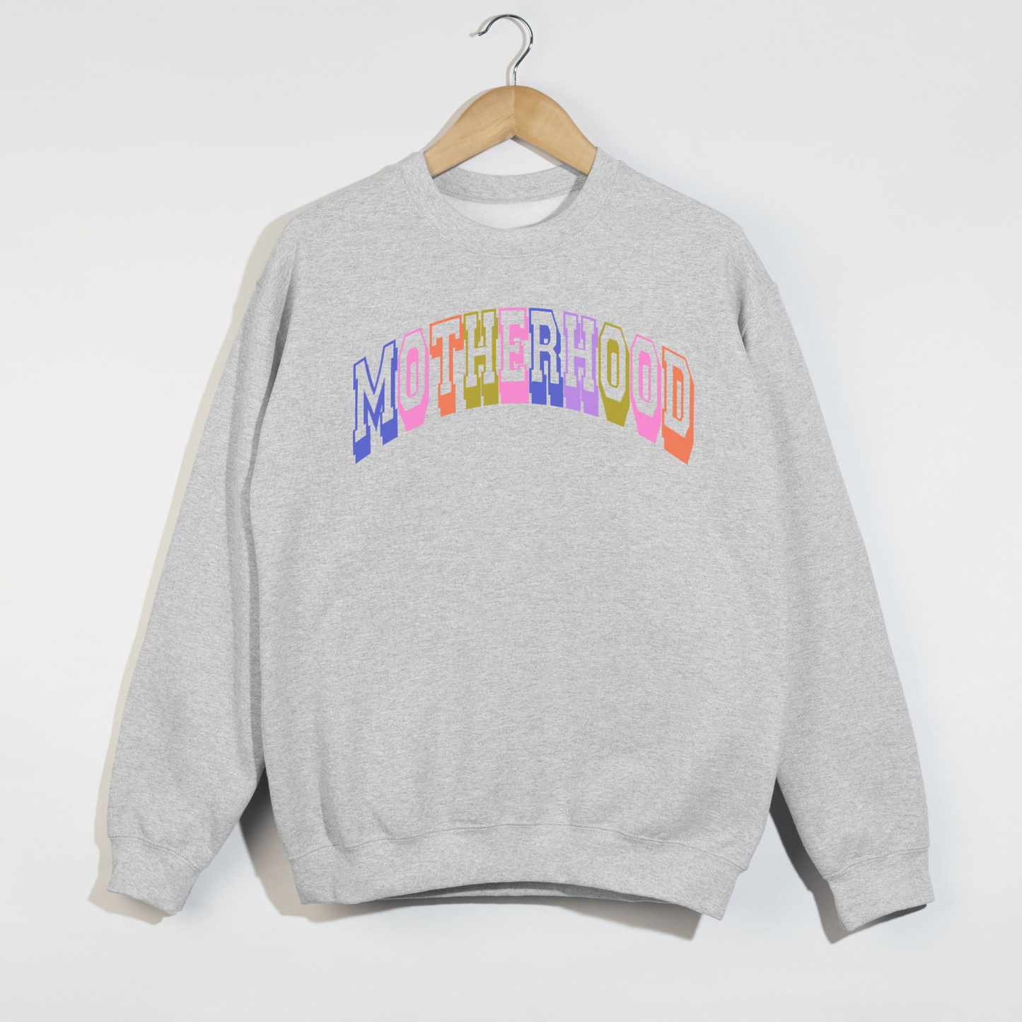 Ash grey retro motherhood graphic sweatshirt with pastel varsity lettering hanging on wooden hanger.