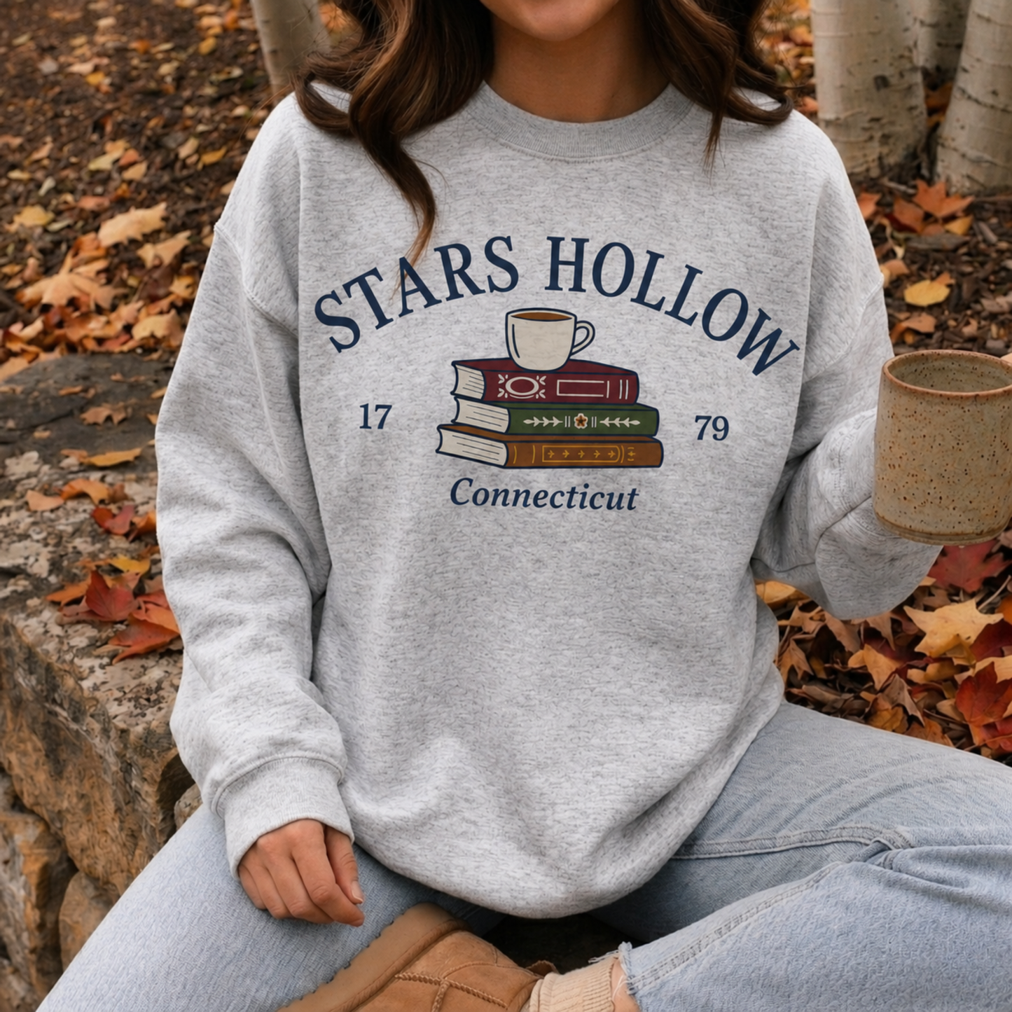 Woman wearing an ash gray Stars Hollow Connecticut sweatshirt while enjoying coffee outdoors during autumn.