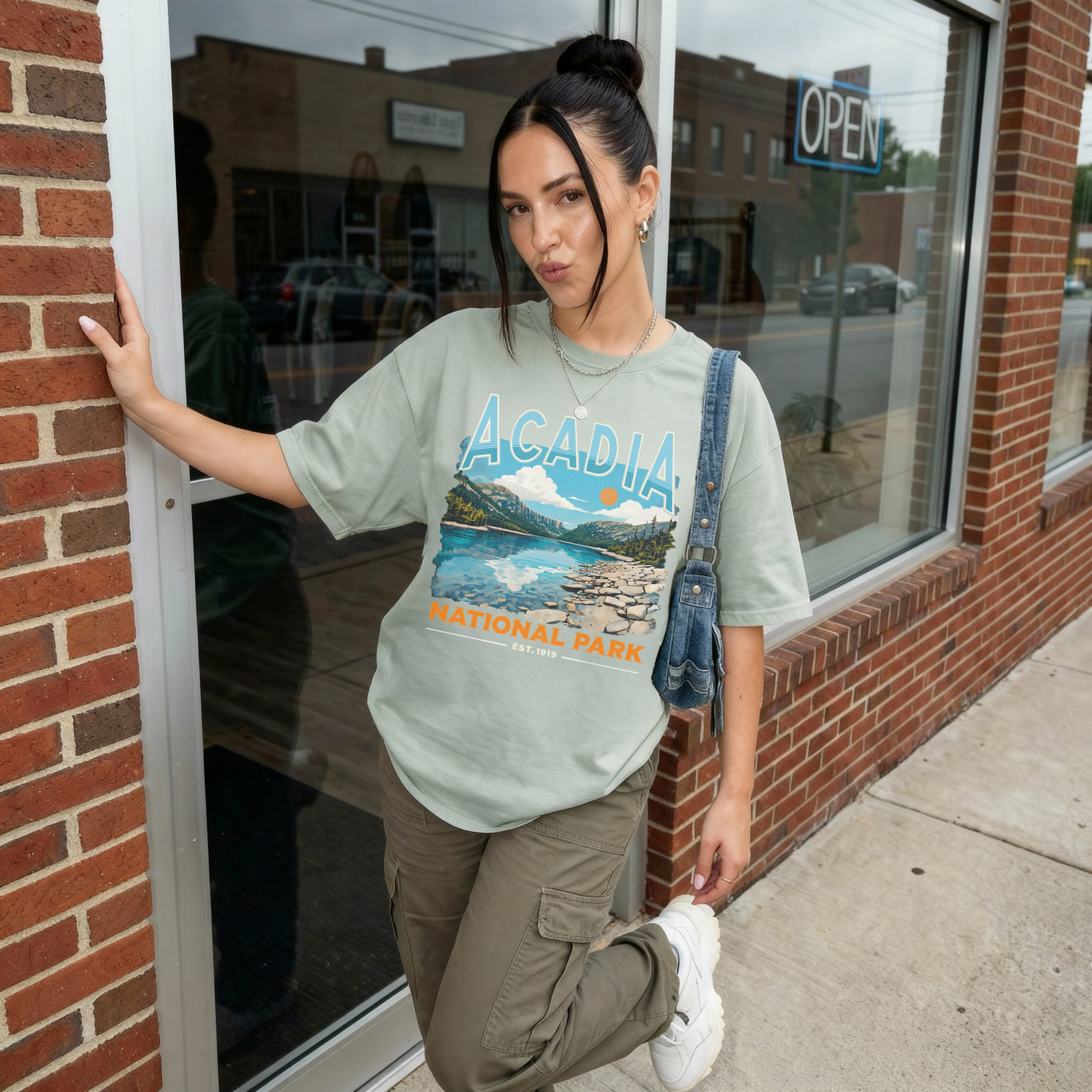 Woman wearing sage green Acadia National Park vintage graphic t-shirt with scenic mountain lake design and retro lettering.