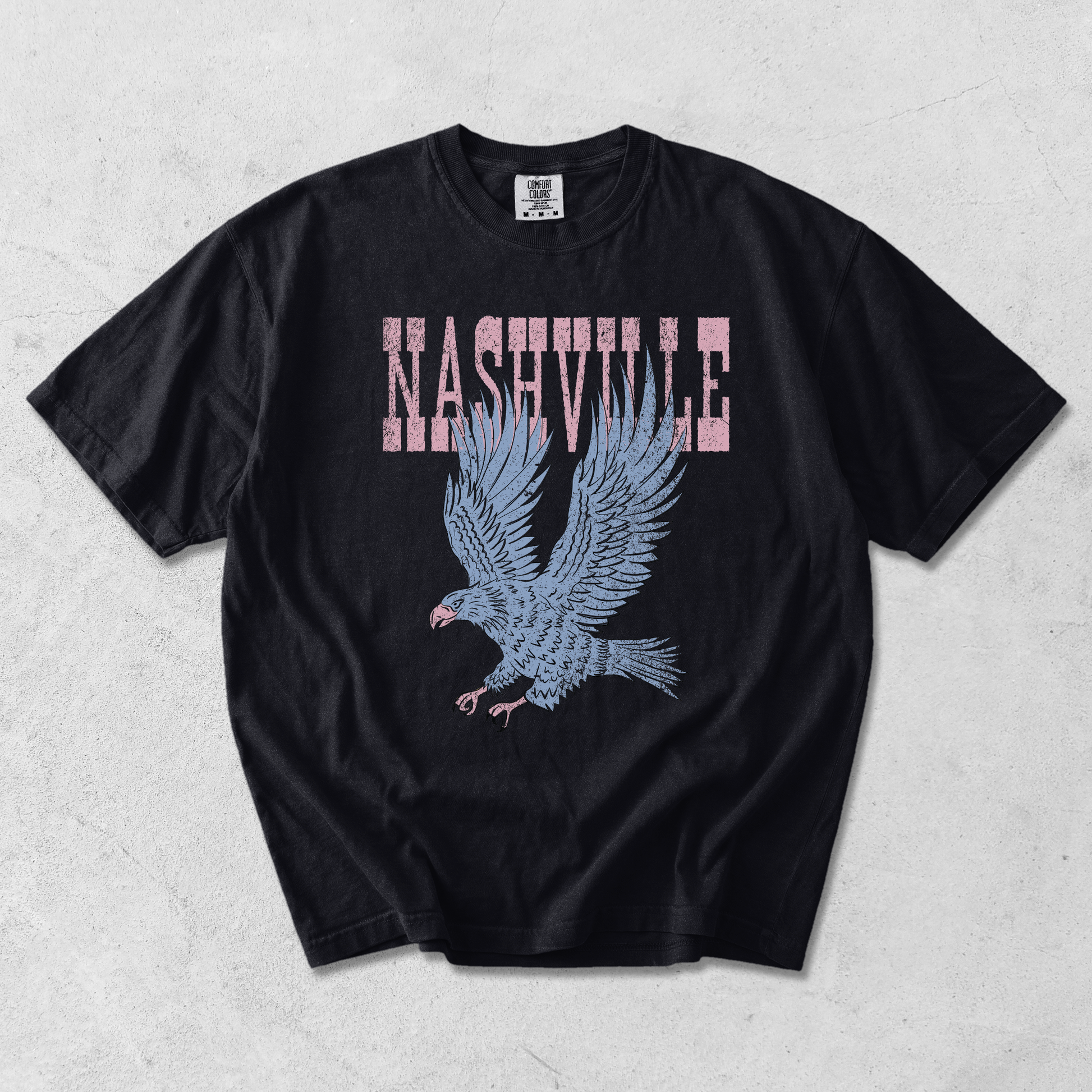 Black Comfort Colors Nashville graphic tee with distressed pink lettering and vintage blue eagle graphic on textured background.