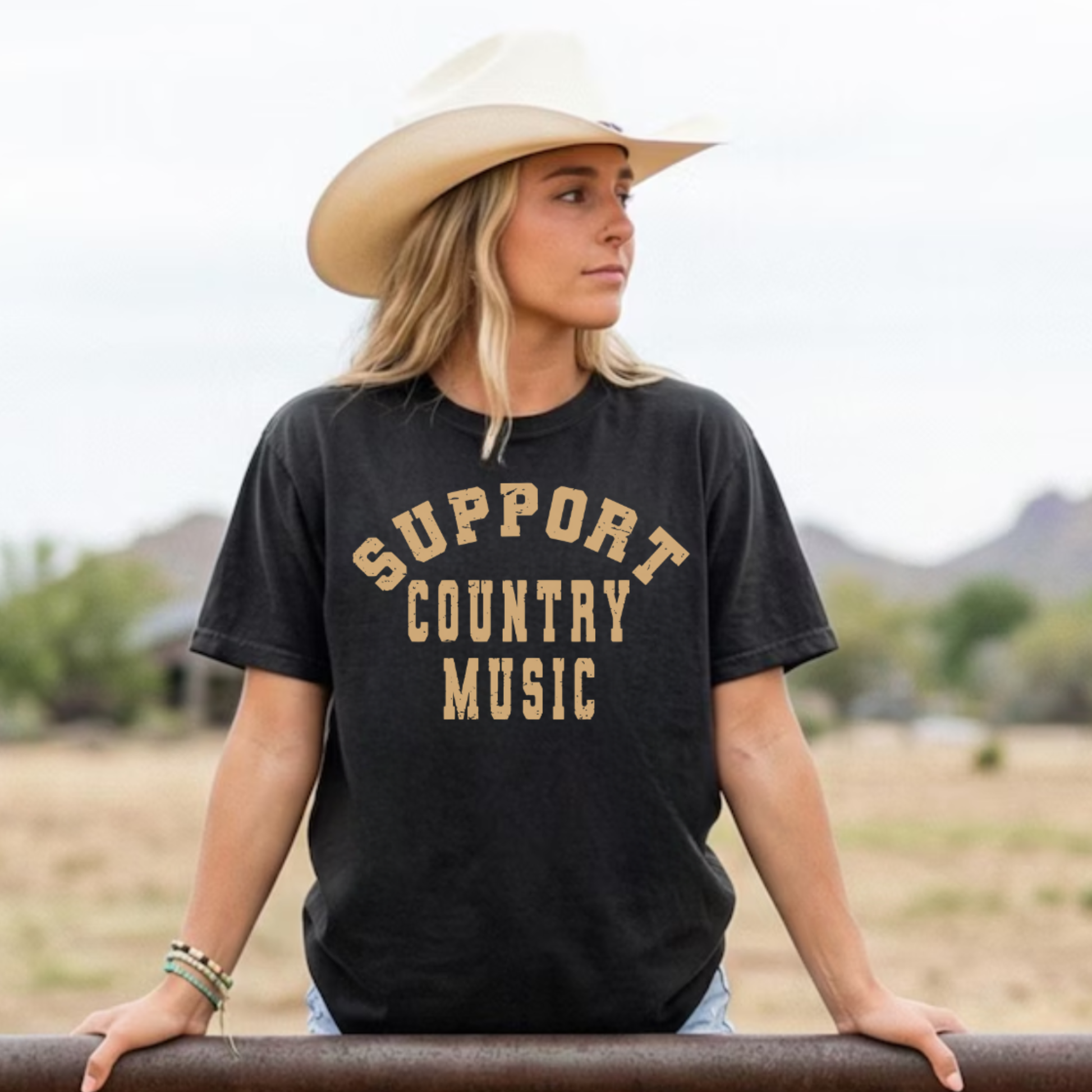 woman in cowboy hat wearing black support country music western graphic tee standing outdoors desert background