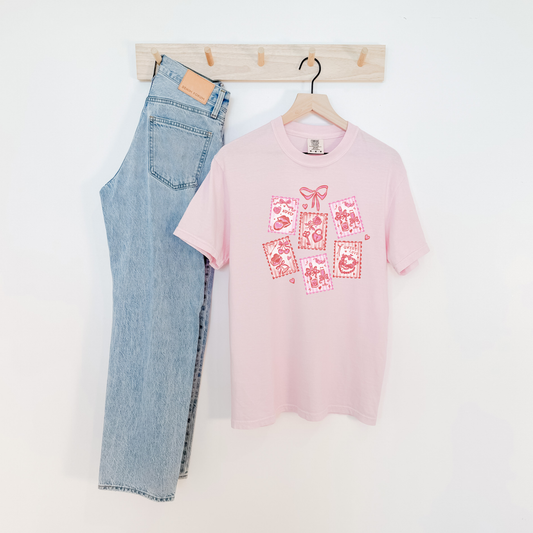 Pink Valentine stamps graphic tee hanging next to denim jeans, girly Valentine t-shirt.