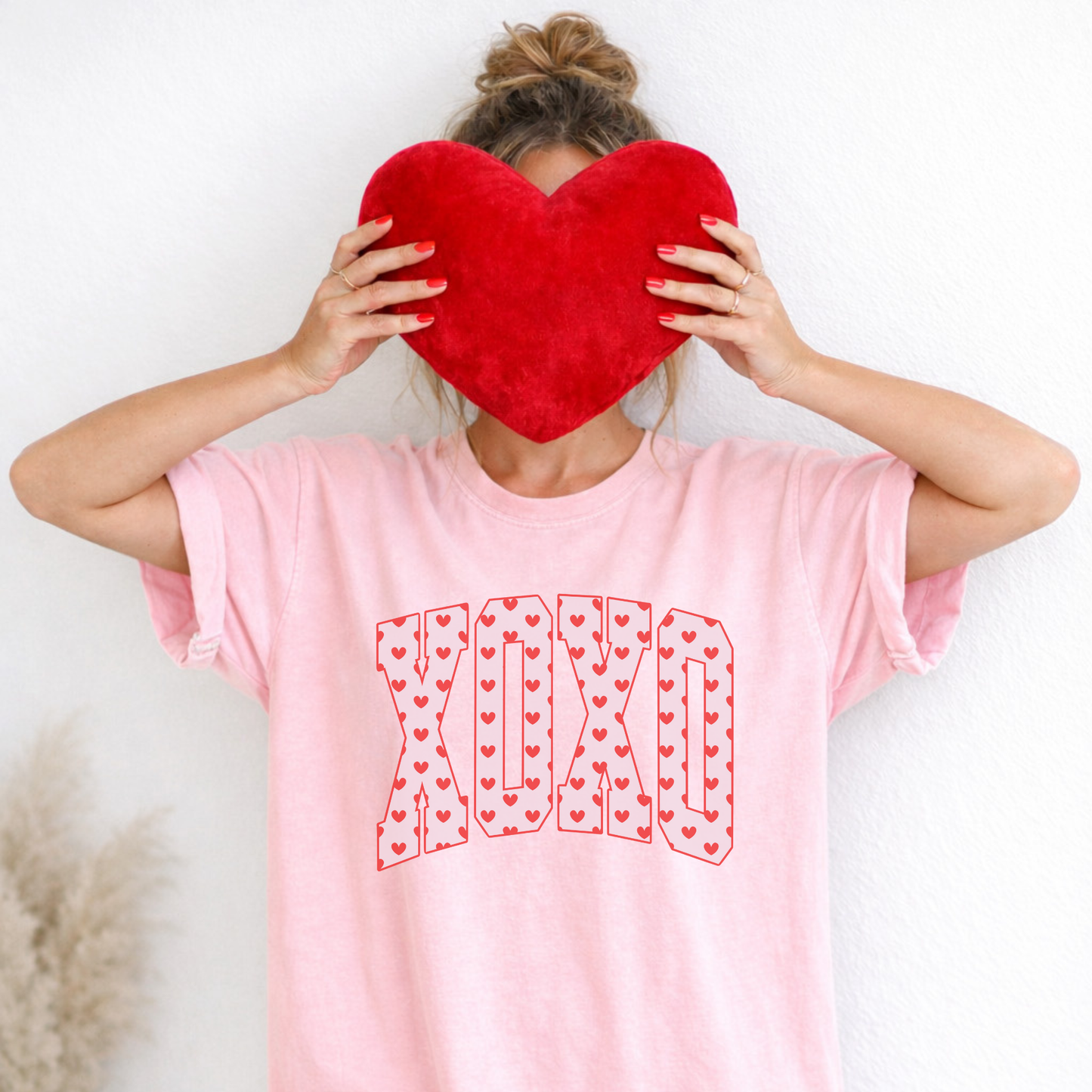 Model wearing blush pink XO heart print Comfort Colors Valentine tee holding red heart