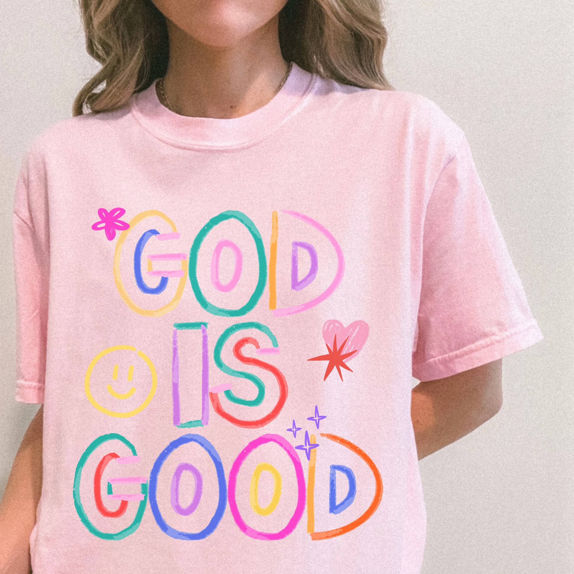 Person wearing a pink t-shirt with 'GOD IS GOOD' in colorful letters.