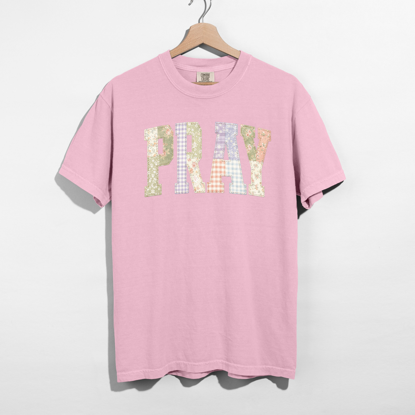 Pink Comfort Colors t-shirt with PRAY printed faux patchwork lettering on hanger