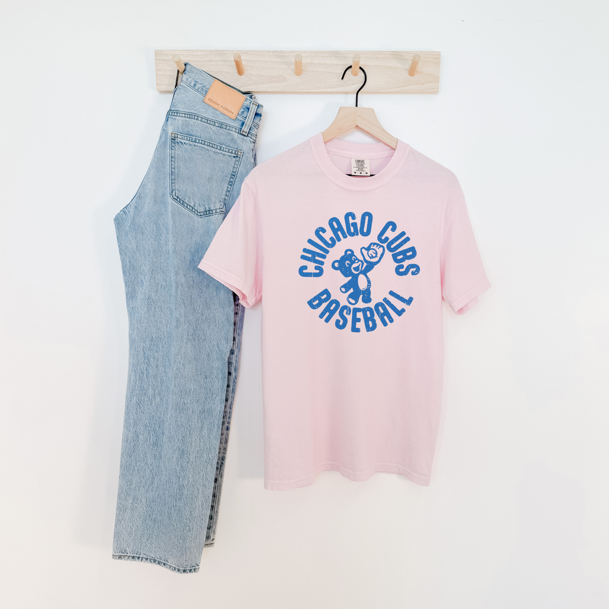 Blush pink Chicago Cubs Baseball retro cub graphic tee hanging next to light wash jeans.