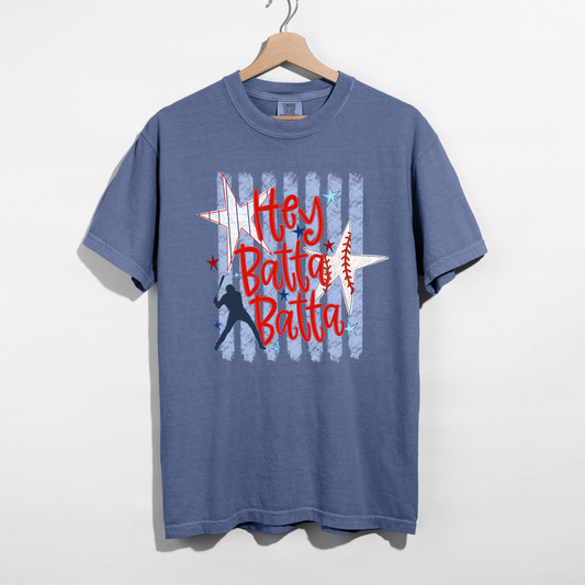 Blue Jean Comfort Colors style baseball graphic t-shirt with Hey Batta Batta red lettering and vintage stripe design hanging on wooden hanger.