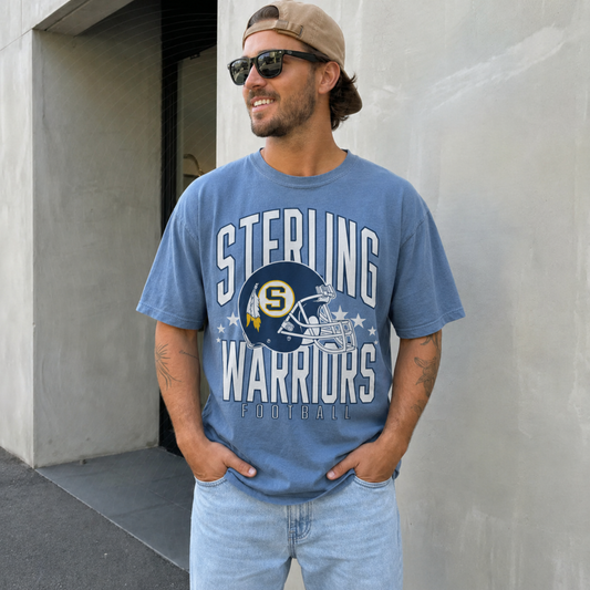 Man wearing a blue jean Sterling Warriors Football graphic t-shirt featuring a vintage football helmet and bold varsity lettering.