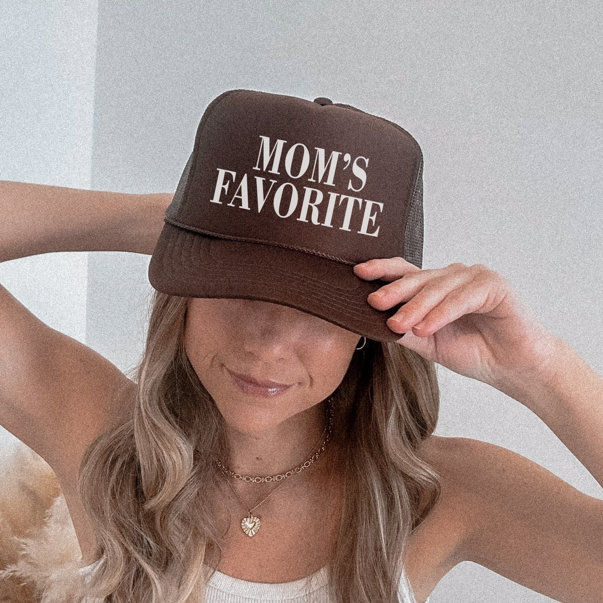 A person wearing a brown trucker hat with 'Mom's Favorite' printed in white text on the front panel.