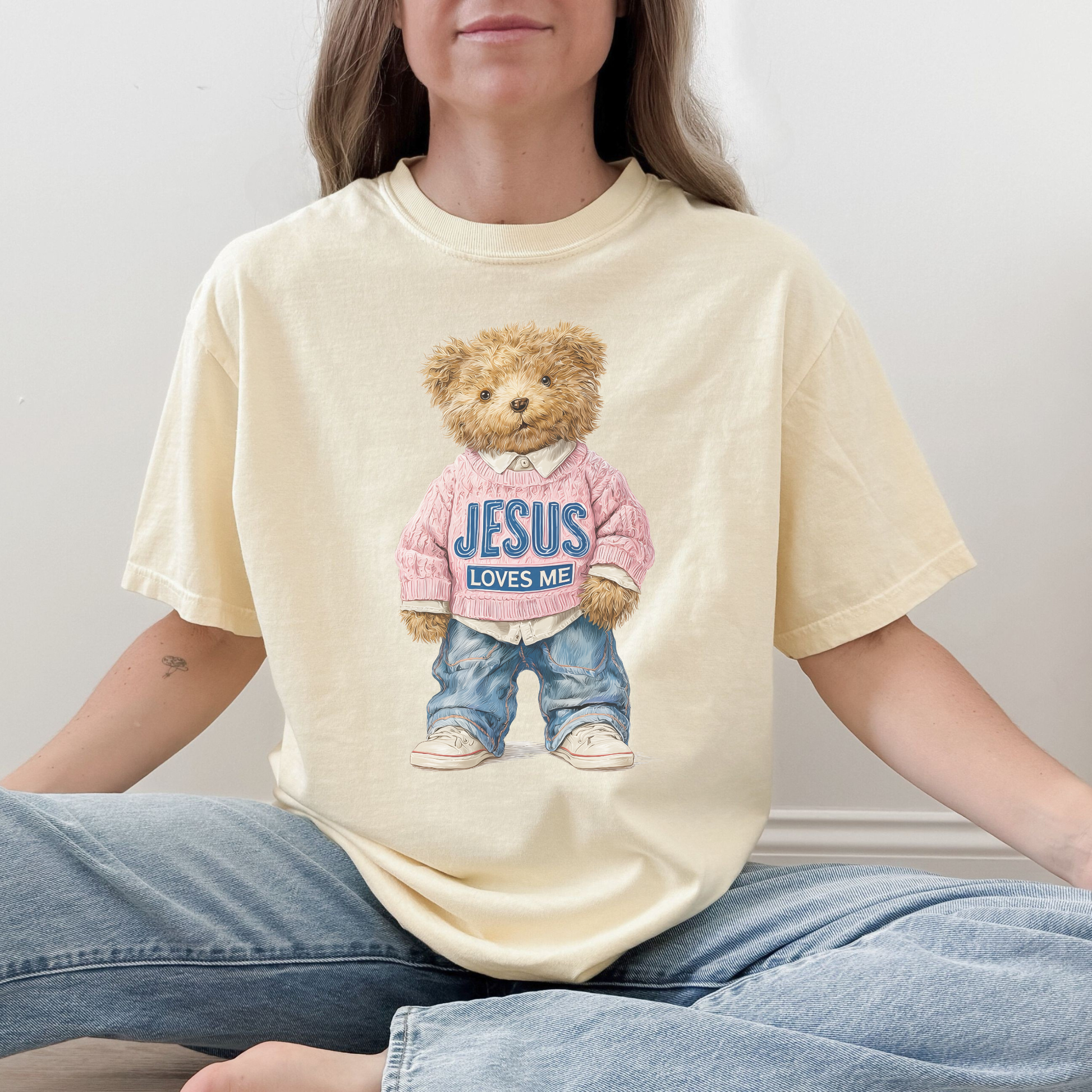 Person wearing a butter t-shirt with a teddy bear graphic and 'Jesus Loves Me' text.