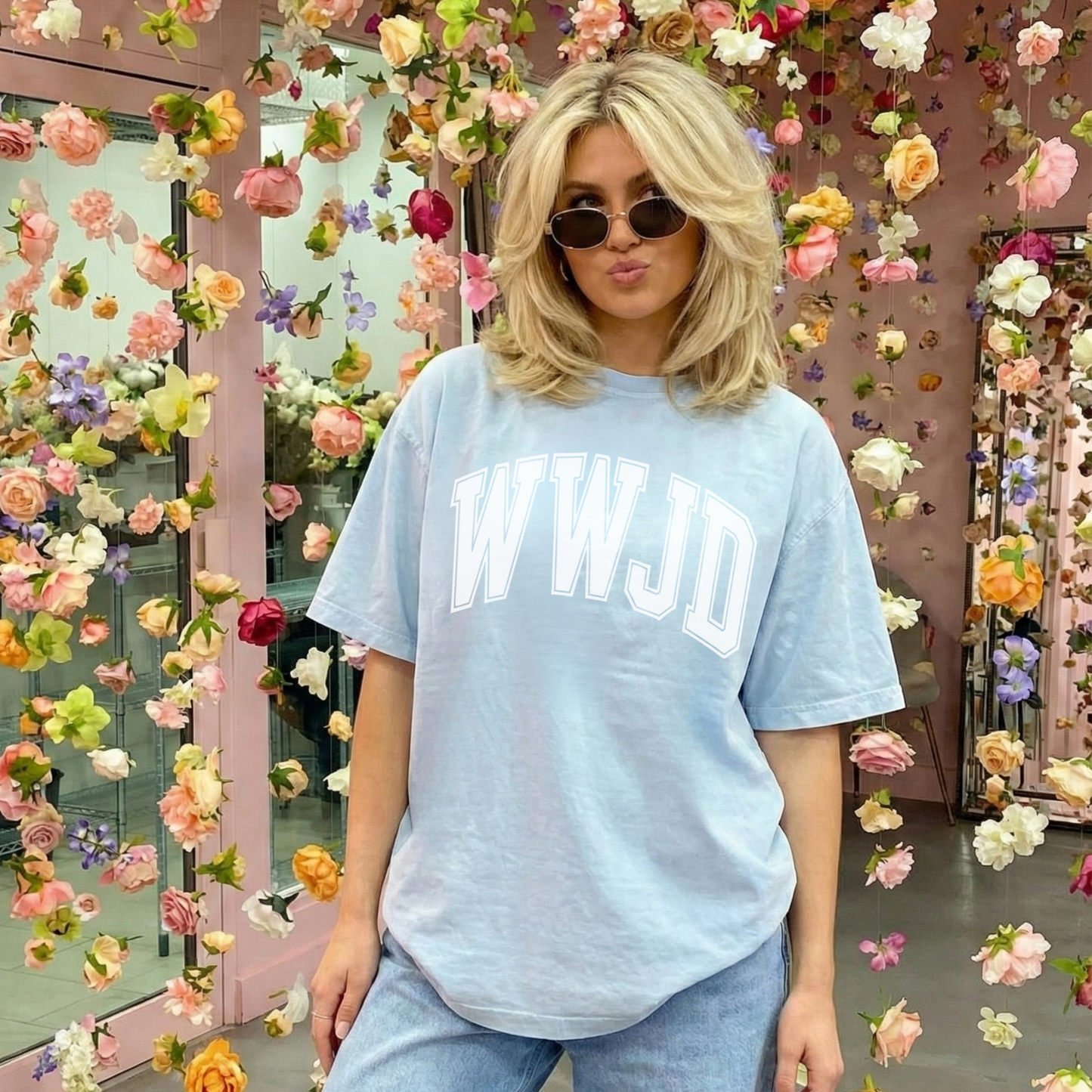 Woman wearing a light blue t-shirt with 'WWJD' text in front of a floral background
