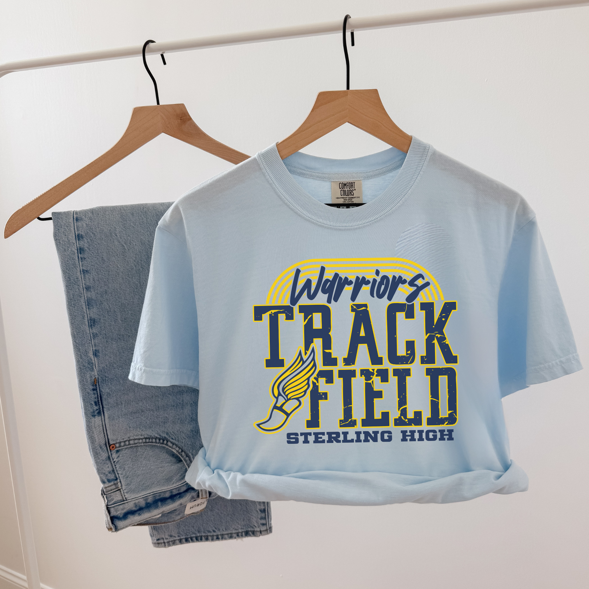 Light blue t-shirt with 'Warriors Track Field Sterling High' design on a hanger against a white background.