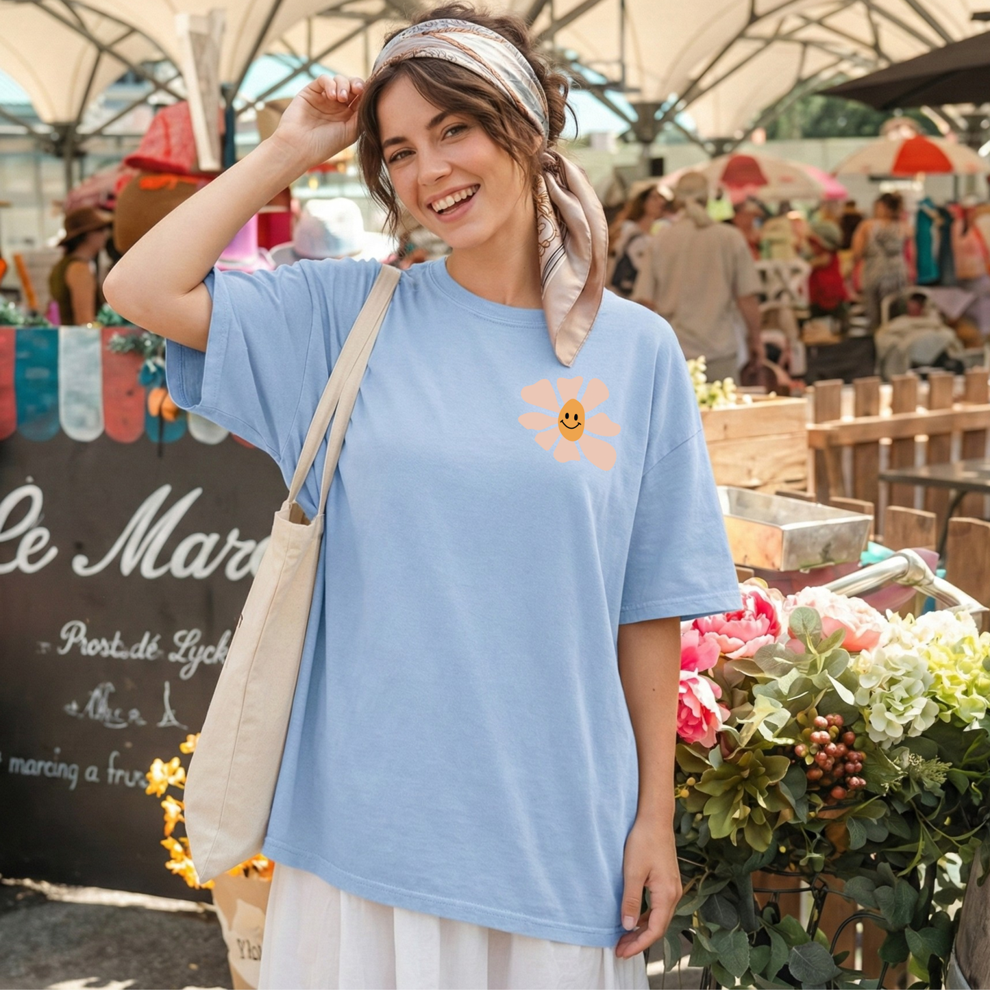 Woman wearing a blue t-shirt with a smiley face design at an outdoor market.