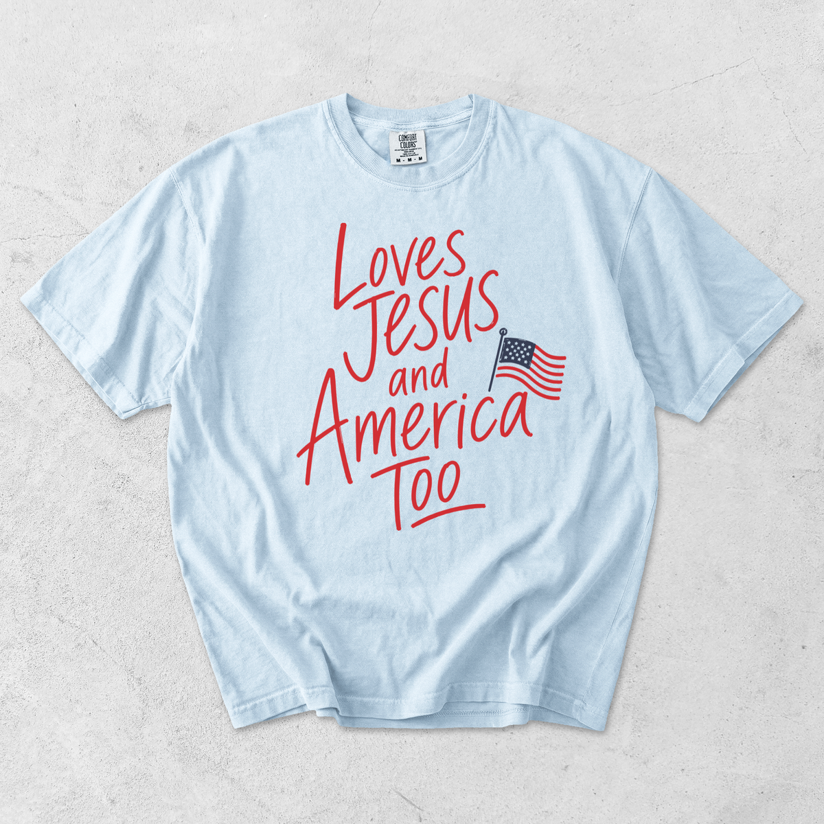 Chambray blue Comfort Colors t-shirt featuring Loves Jesus and America Too patriotic Christian graphic with American flag
