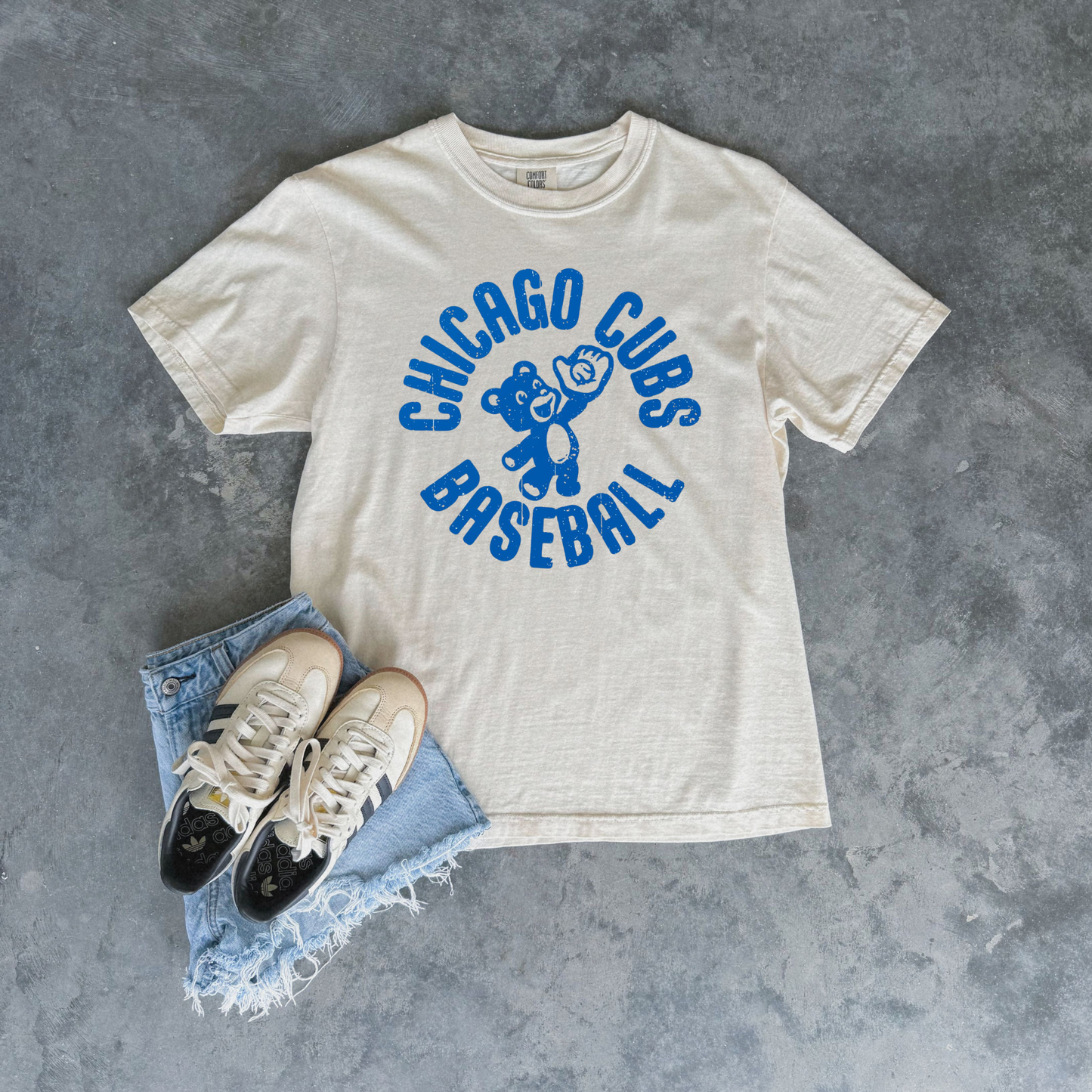 Ivory Chicago Cubs Baseball graphic t-shirt with distressed blue retro cub design styled with denim shorts and sneakers.