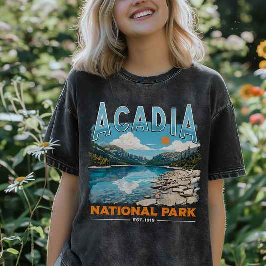Woman wearing black mineral wash Acadia National Park graphic t-shirt with vintage mountain lake design in garden setting.