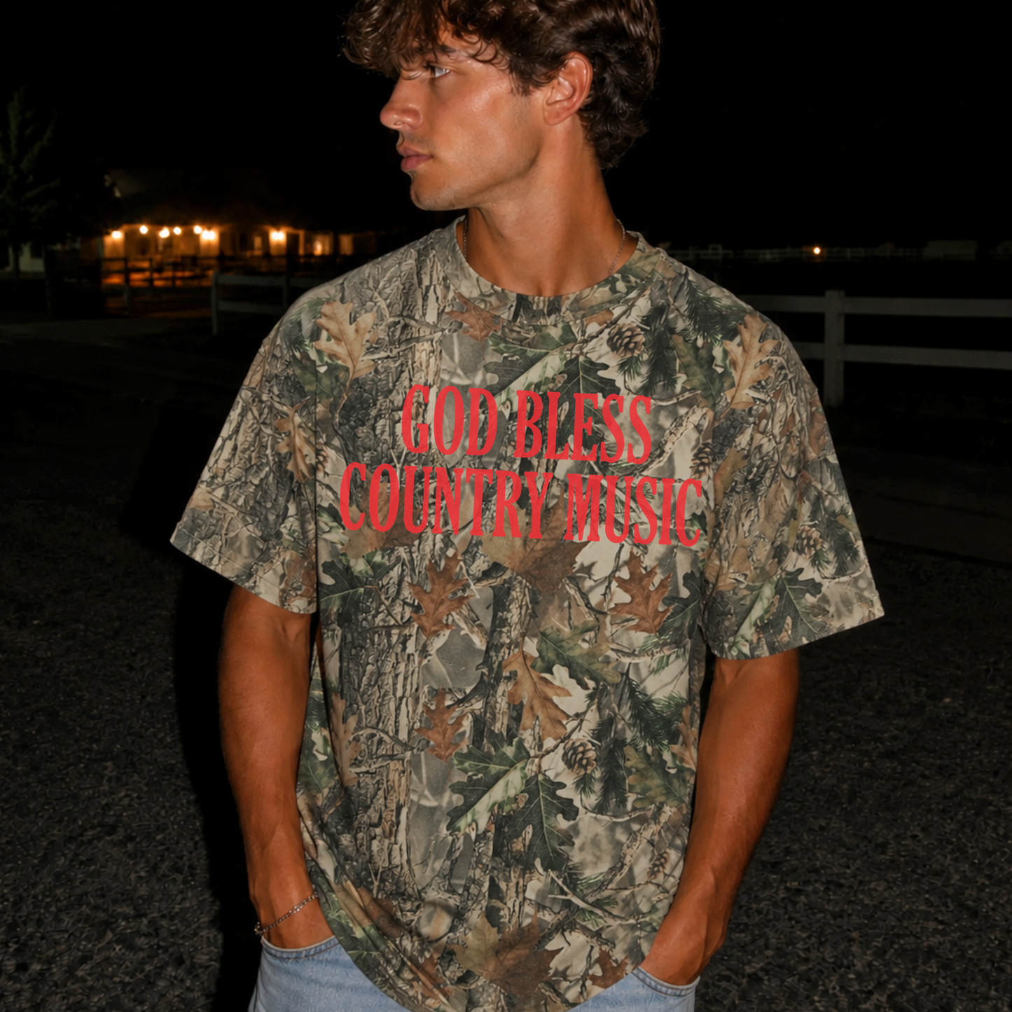 Man wearing an oversized vintage wood camouflage graphic tee featuring a red "God Bless Country Music" graphic, styled casually for a rugged western outdoor look.